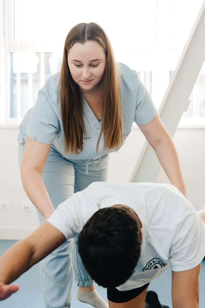 A physiotherapist assists a client in an exercise during a therapy session indoors.